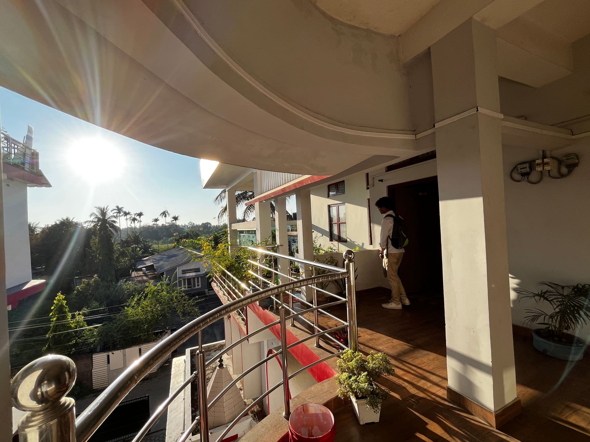 Covered balcony walkway with wooden floors and a sunlit view of the trees